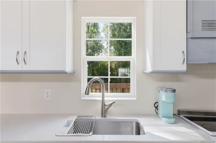 Kitchen Sink &amp; Window – Stainless-steel sink w/pull-down faucet, solid surface countertop &amp; window overlooking the greenery outside.