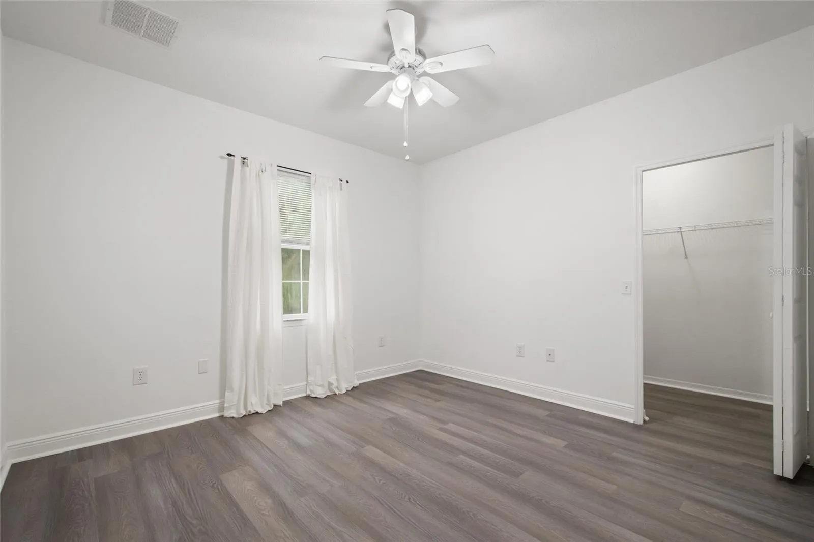 Bedroom 2 with a walk in closet, ceiling fan, drapery rod (drapes do not convey) as well as it is finished in the same luxury plank vinyl.