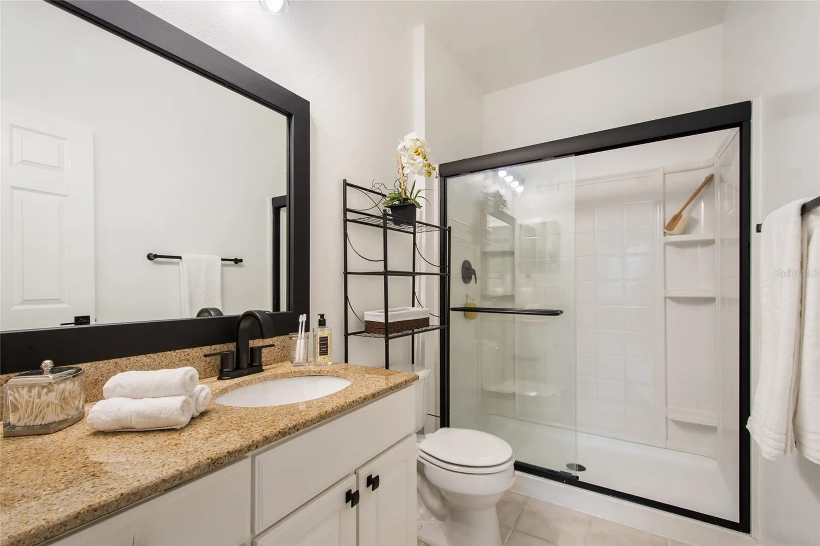 The primary bathroom is totally updated Granite countertops, new moen faucet and shower fixtures, newly framed and painted mirror, new tollet paper holder and completed by a towel bar. The glass shower door is trimmed in black finish to match the balance of the bathroom. Note the new cabinet hardware and the over the toilet storage system that comes with the unit.