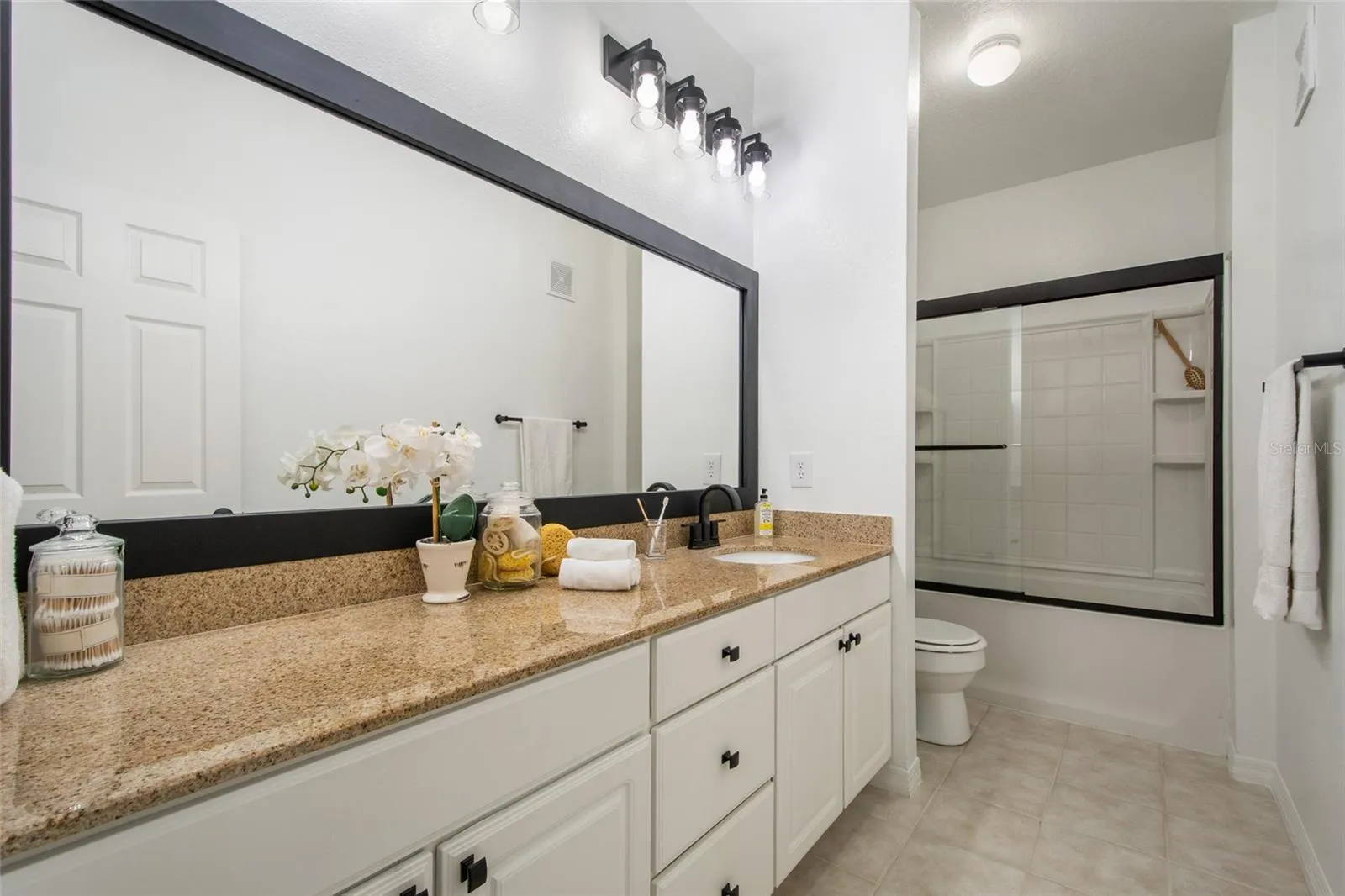 The supporting bathroom between bedrooms 2 and 3 features a elongated vanity with plenty of storage, new MOEN faucet and tub/shower plumbing fixtures, granite countertop, newly framed and painted mirror and brand new light fixtures, toilet paper holder and a convenient towel bar complete this spacious bathroom. Note also the framed glass shower door and built in shower shelving for all your bathroom supplies.