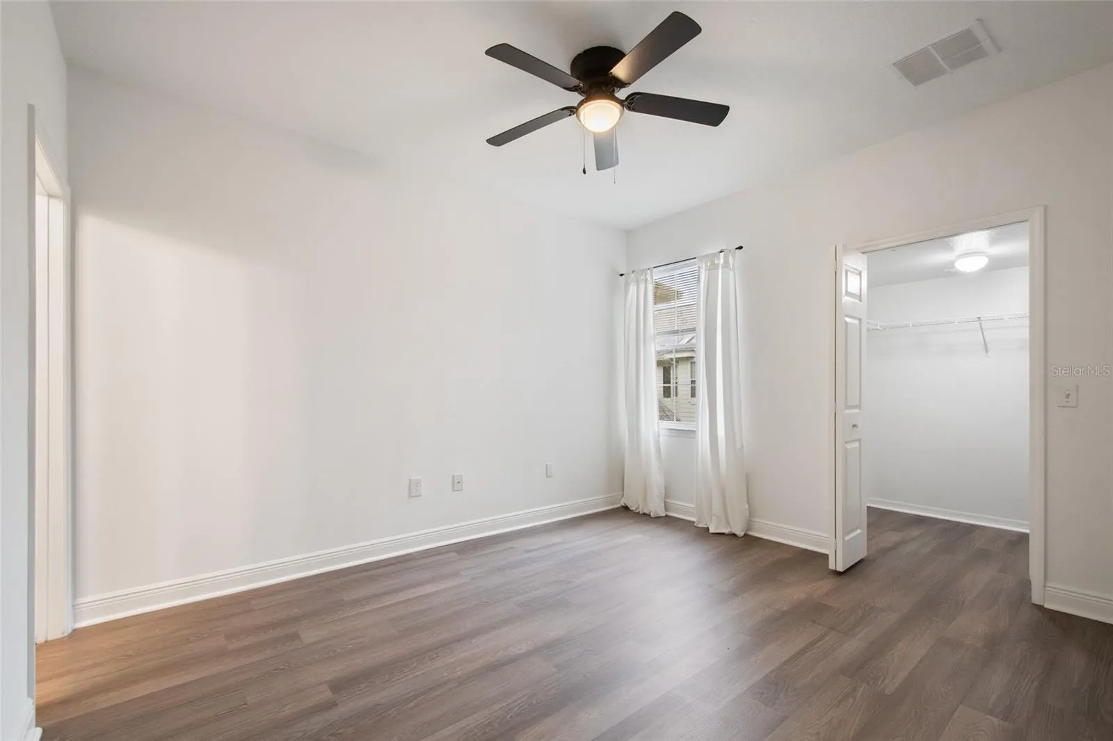 An alternate view of the primary suite looking towards the walk in closet and window which has a lovely view of the surrounding area and allows natural light to flood the room.