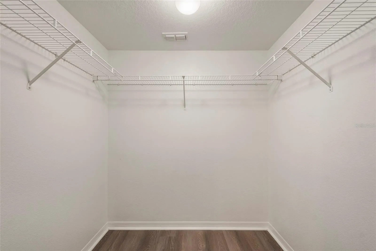 Primary suite closet equipped with light, shelving and finished with luxury plank vinyl flooring.