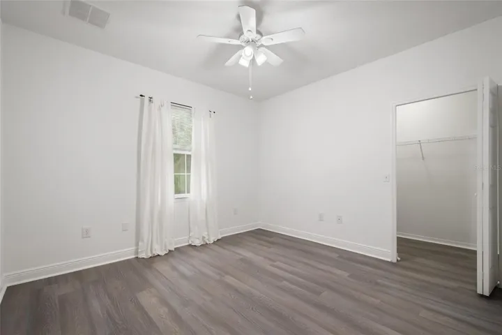 Bedroom 2 with a walk in closet, ceiling fan, drapery rod (drapes do not convey) as well as it is finished in the same luxury plank vinyl.