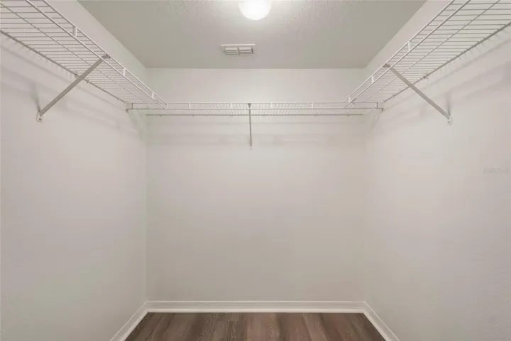 Primary suite closet equipped with light, shelving and finished with luxury plank vinyl flooring.