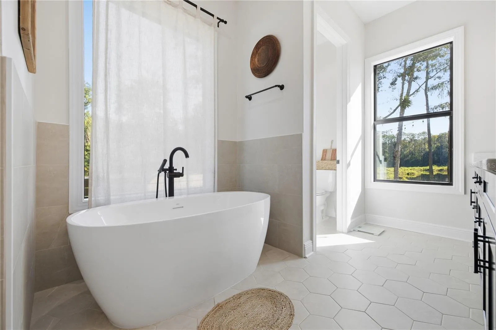 Freestanding soaking tub in the primary bath with tile up half of the surrounding wall with large window for natural light and embracing the privacy of your property.