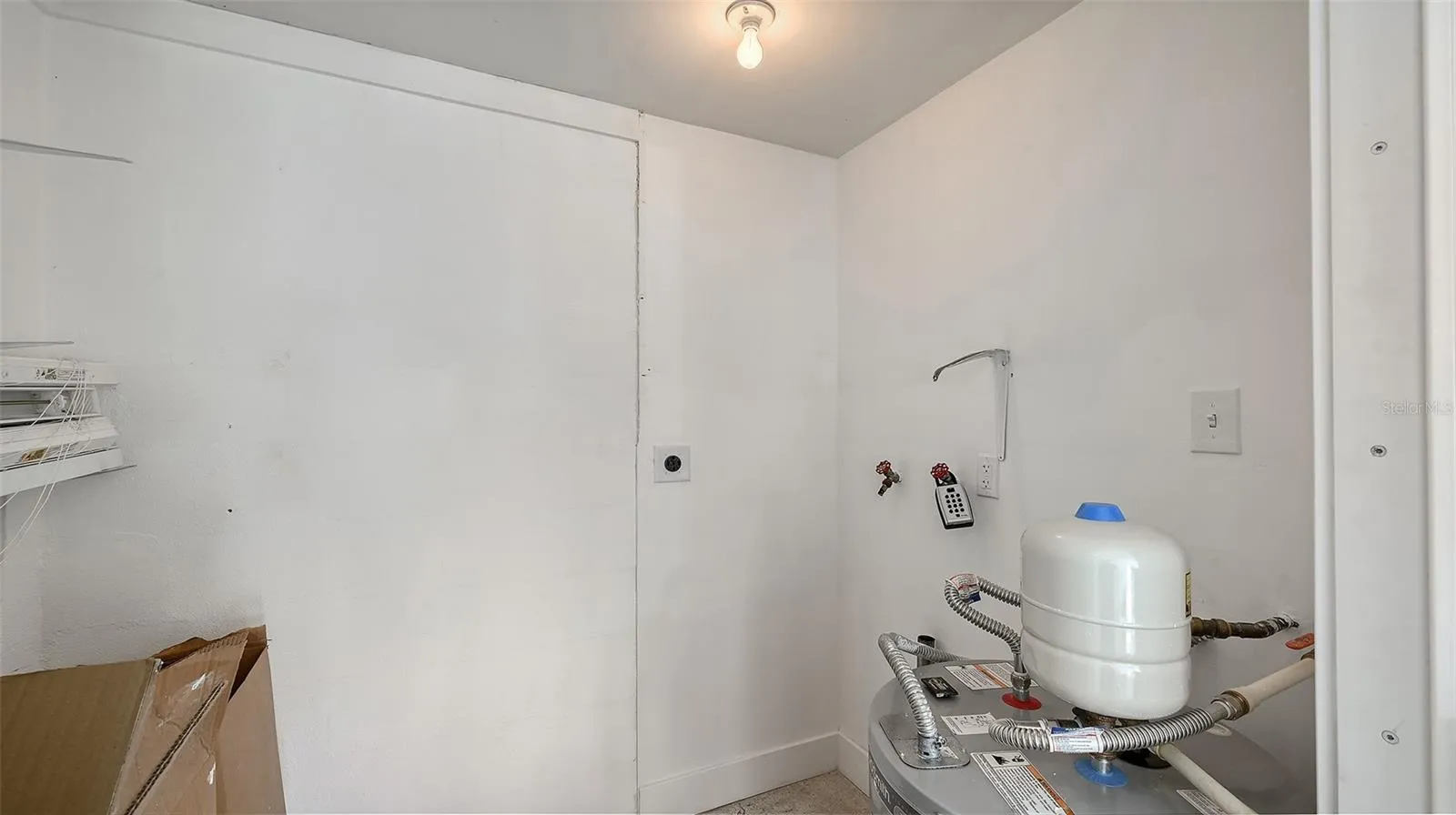 The storage room behind the carport with the new water heater and previous washer/dryer hookup.