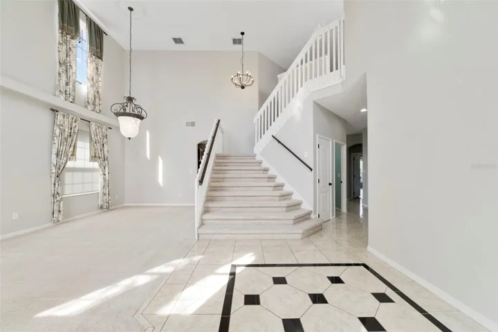 Inside, ETCHED-GLASS FRENCH DOORS open to a welcoming foyer with a SOARING CEILING and decorative tile flooring, setting the stage for the generous living spaces beyond.