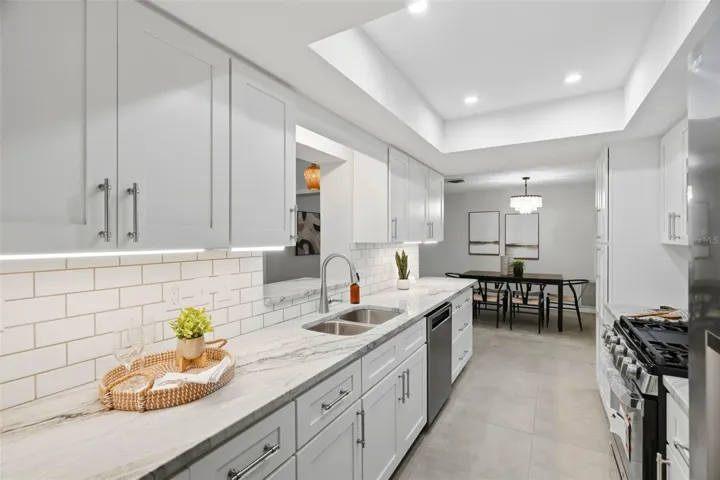 Anchoring the home is a centrally located kitchen featuring classic white shaker-style cabinetry, a subway tile backsplash, stone countertops, and a tray ceiling with recessed lighting.