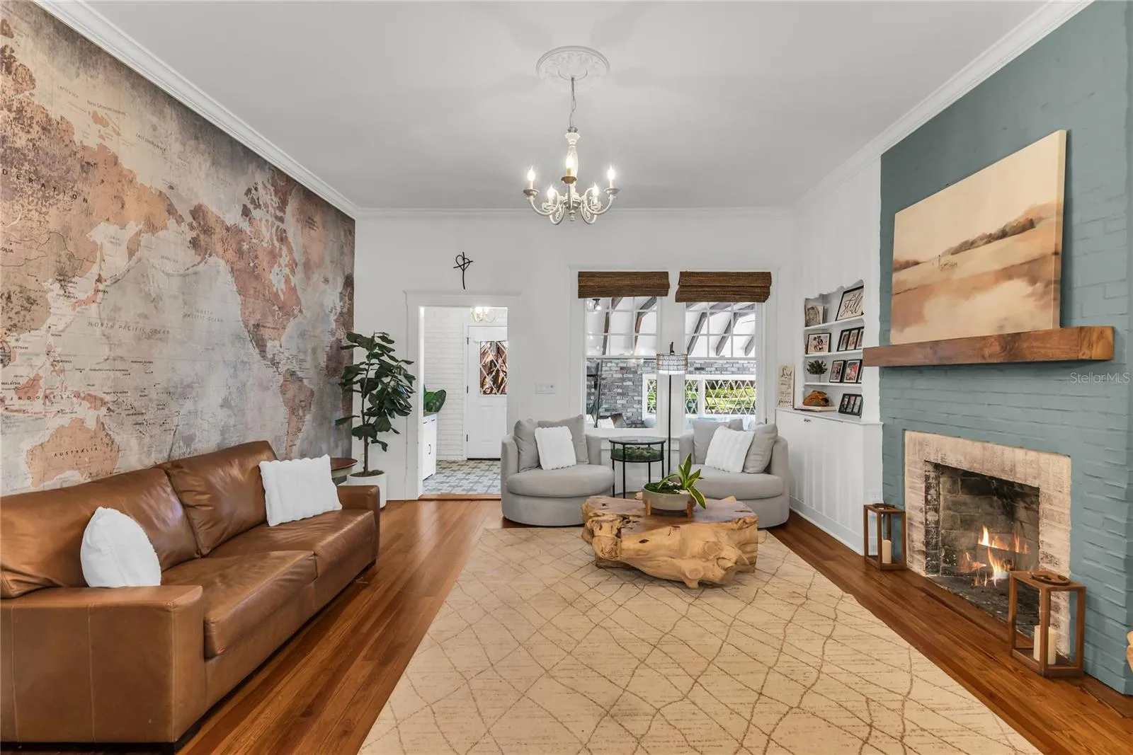 The warm and welcoming Formal Living Room is anchored by a wood-burning brick fireplace accented by a substantial wood mantle and custom painted brick. A custom built in shelf, original wood flooring and chandelier preserve the homes original historic charm and a world map accent wall adds personality. The spacious layout offers a seamless connection to the adjoining dining room and kitchen, creating an effortless flow throughout the home's main living spaces.