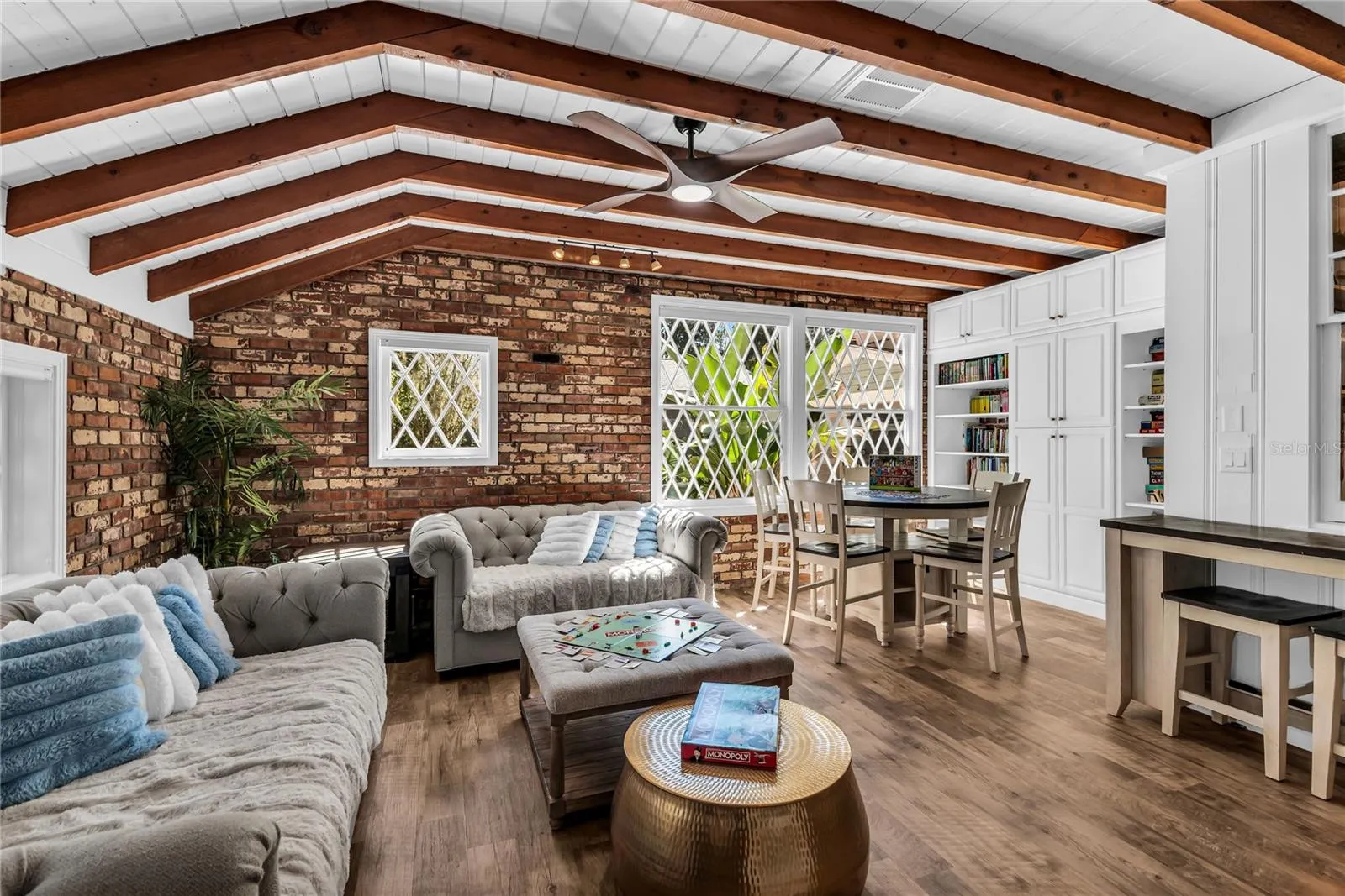 Natural light pours into the spacious family room that features warm brick walls, exposed wood beams and distinctive diamond-pane windows that create a timeless architectural backdrop.