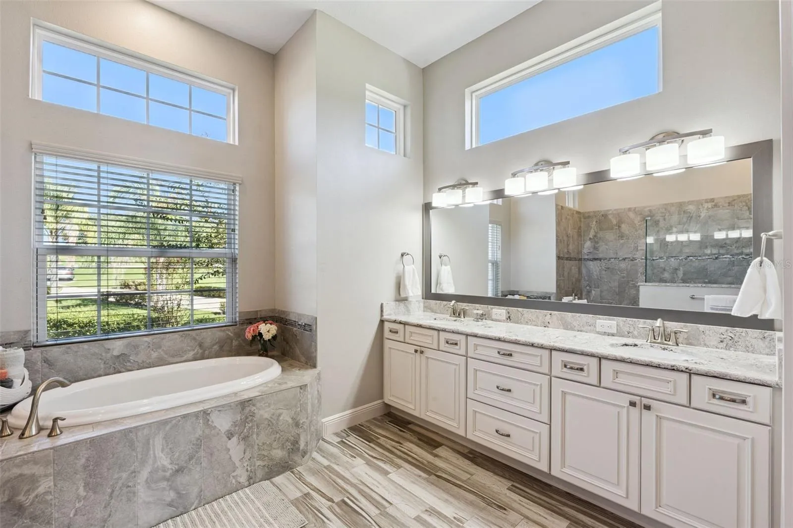Light-filled primary en suite featuring elegant oversized windows, high-end lighting fixtures, and sleek quartz countertops.