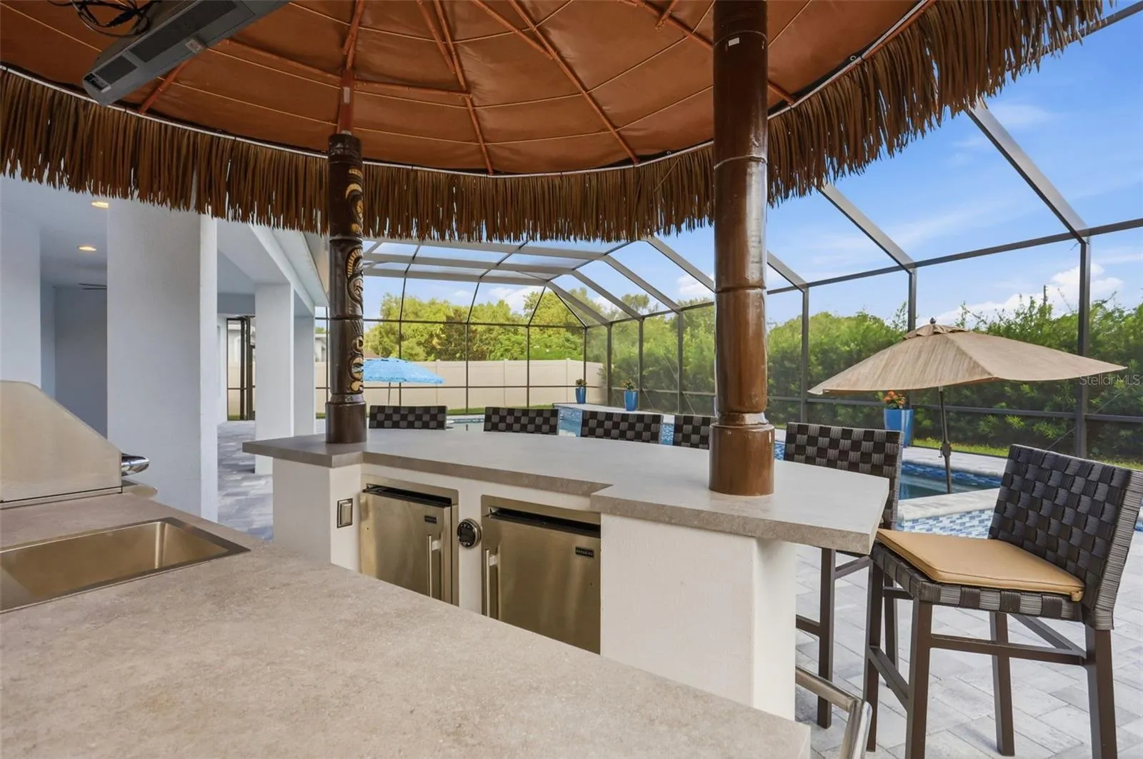 Summer kitchen includes a grill, two refrigerators, large entertaining bar, and remote pull down TV