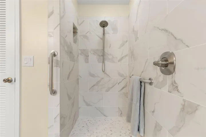 A closer look at the beautifully updated primary shower reveals striking tile, a pebble-style floor, built-in niche, and handheld showerhead, creating a refreshing escape with a touch of modern elegance.