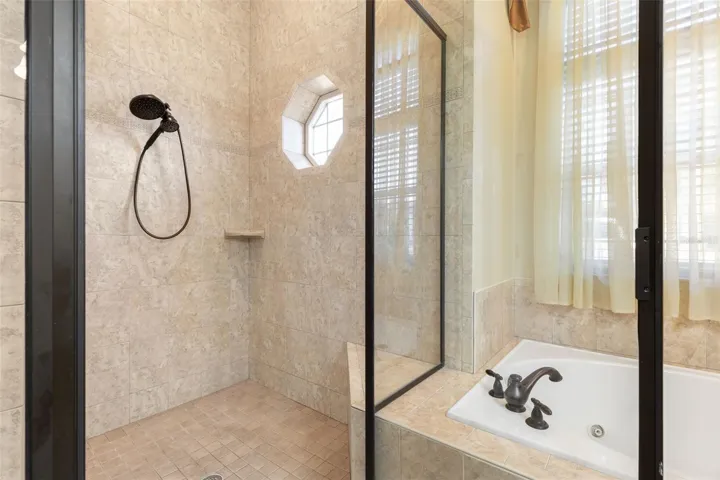 A spacious, tiled walk-in shower featuring glass enclosure, handheld showerhead, and a distinctive octagonal window.