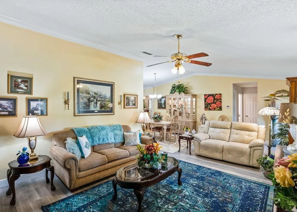 Inviting living area featuring wood-look vinyl flooring, crown molding, soft neutral walls, and a ceiling fan. The open layout connects seamlessly to the dining area, creating a comfortable space for everyday living and entertaining.