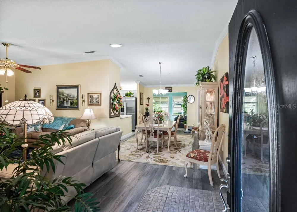 Welcoming entry opens to a bright living and dining area featuring wood-look vinyl flooring, crown molding, and soft neutral tones. The open layout offers an inviting flow, with views toward the kitchen and sunlit rear living space.