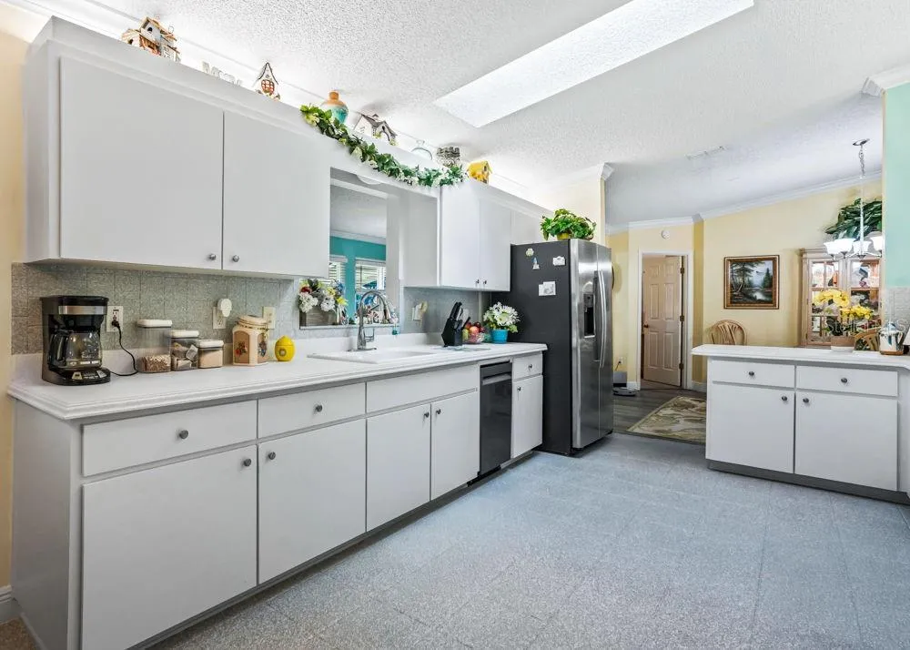Bright, spacious kitchen featuring abundant white cabinetry, generous counter space, stainless steel appliances, and a double-basin sink. A skylight adds natural light, while the open connection to the dining area makes serving and entertaining convenient.