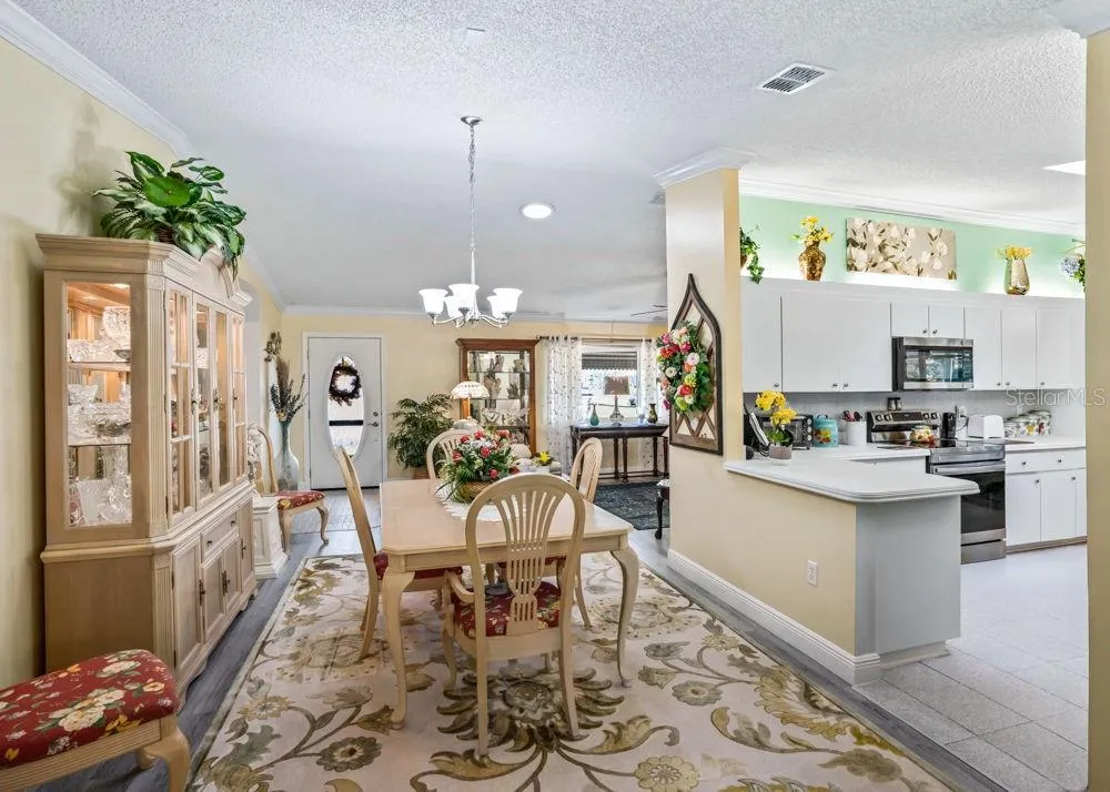 Inviting dining space with wood-look flooring, crown molding, and chandelier lighting opens to the living room and kitchen.