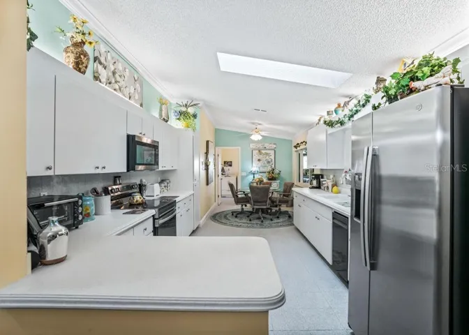 Bright kitchen featuring white cabinetry, stainless steel appliances, ample counter space, and a convenient breakfast bar. A skylight brings in natural light, while the adjoining breakfast nook offers a comfortable spot for casual dining.
