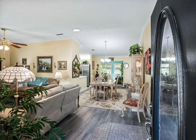 Welcoming entry opens to a bright living and dining area featuring wood-look vinyl flooring, crown molding, and soft neutral tones. The open layout offers an inviting flow, with views toward the kitchen and sunlit rear living space.