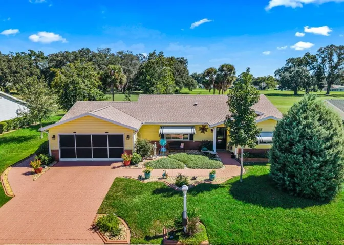 Welcome to this charming 2-bedroom, 2-bathroom home featuring cheerful yellow siding, a brick-paver driveway and walkway, screened garage, and a covered front porch. Mature trees, manicured landscaping, and golf course views create a picturesque Florida setting.