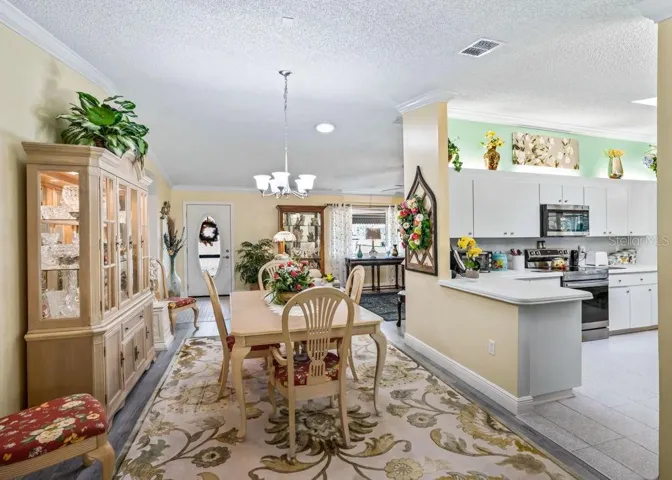 Inviting dining space with wood-look flooring, crown molding, and chandelier lighting opens to the living room and kitchen.