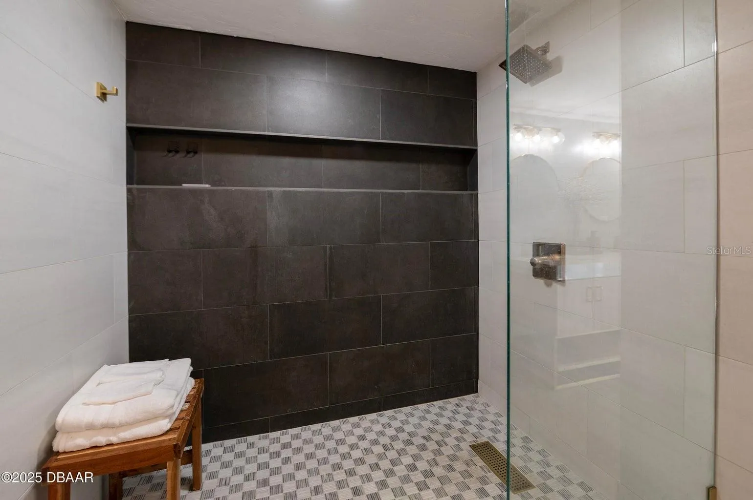 : This spacious walk-in shower features a striking dark tile accent wall, contrasting light tile surrounds, a rainfall showerhead, built-in storage niche, and sleek glass partition for a contemporary, spa-inspired feel.