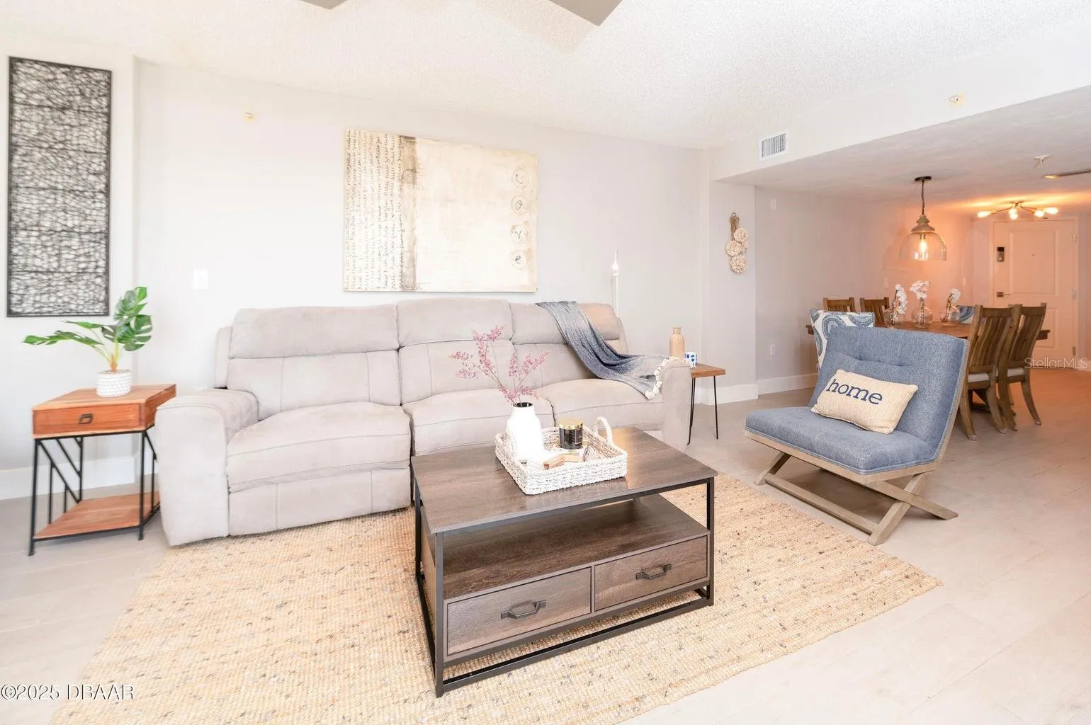 This inviting living room offers a comfortable gathering space with neutral finishes and an open connection to the dining area, ideal for relaxing after a day at the beach.