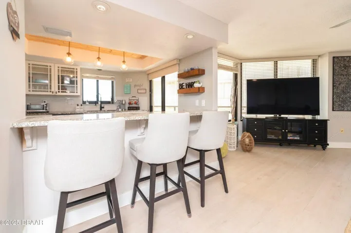 The kitchen flows effortlessly into the living area, with a spacious breakfast bar, contemporary lighting, and large windows creating a comfortable setting for everyday living and entertaining.