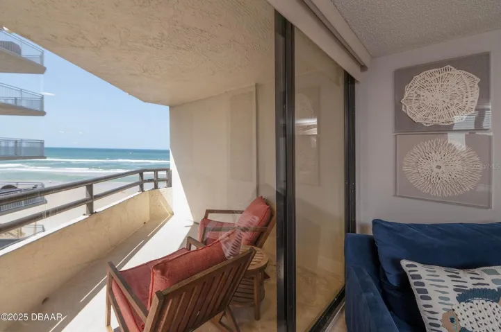 Floor-to-ceiling sliding glass doors connect the living room to the covered oceanfront balcony, offering an effortless transition between indoor comfort and outdoor relaxation.