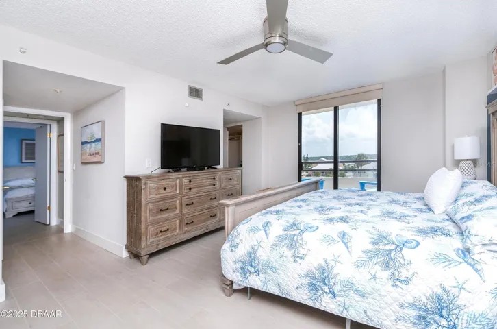 Another view of the generously sized primary bedroom showcases abundant natural light, neutral finishes, and direct balcony access, creating a comfortable coastal retreat.