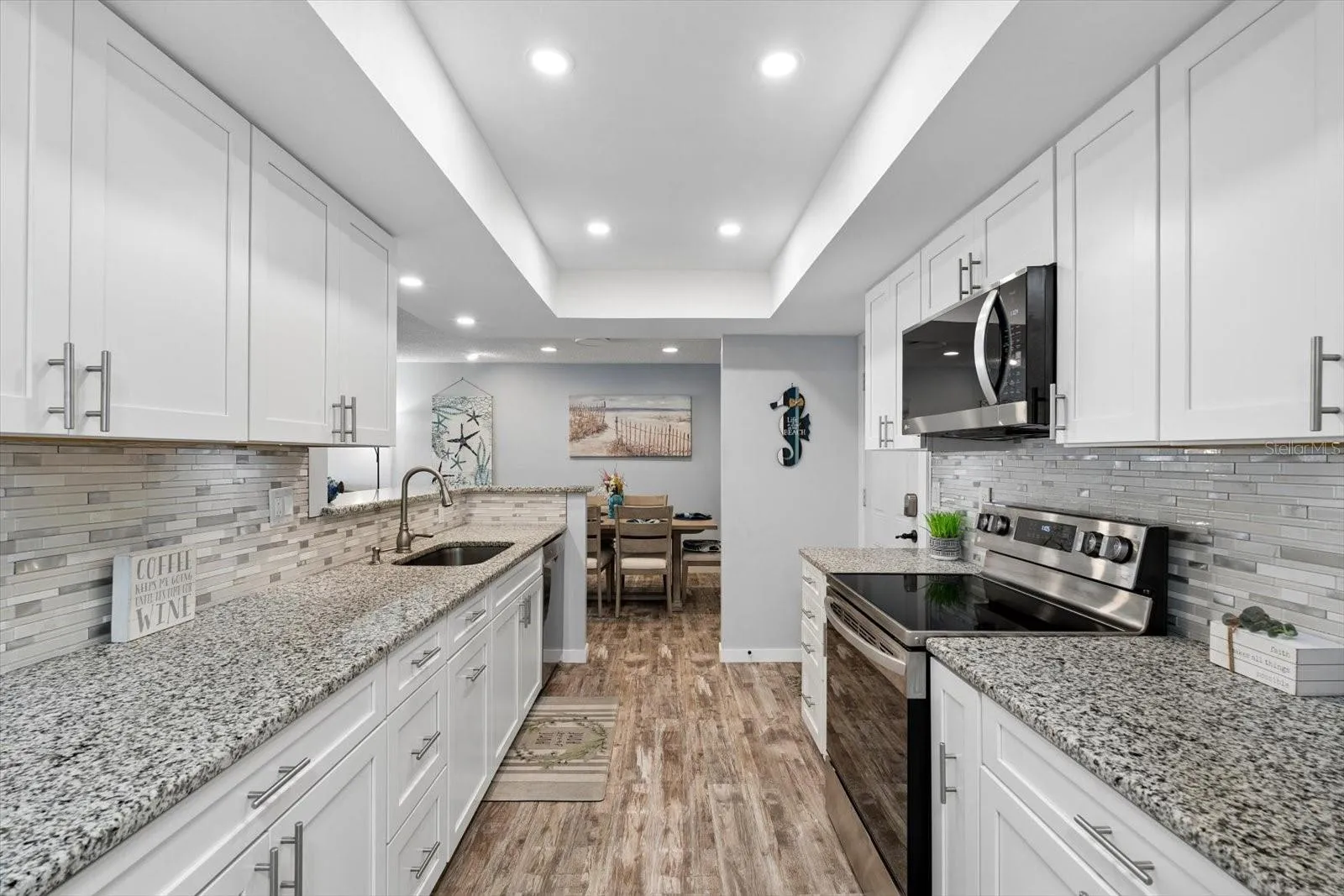 Gorgeous open kitchen with stainless steel appliances, white shaker cabinets, granite countertops, recessed lighting.