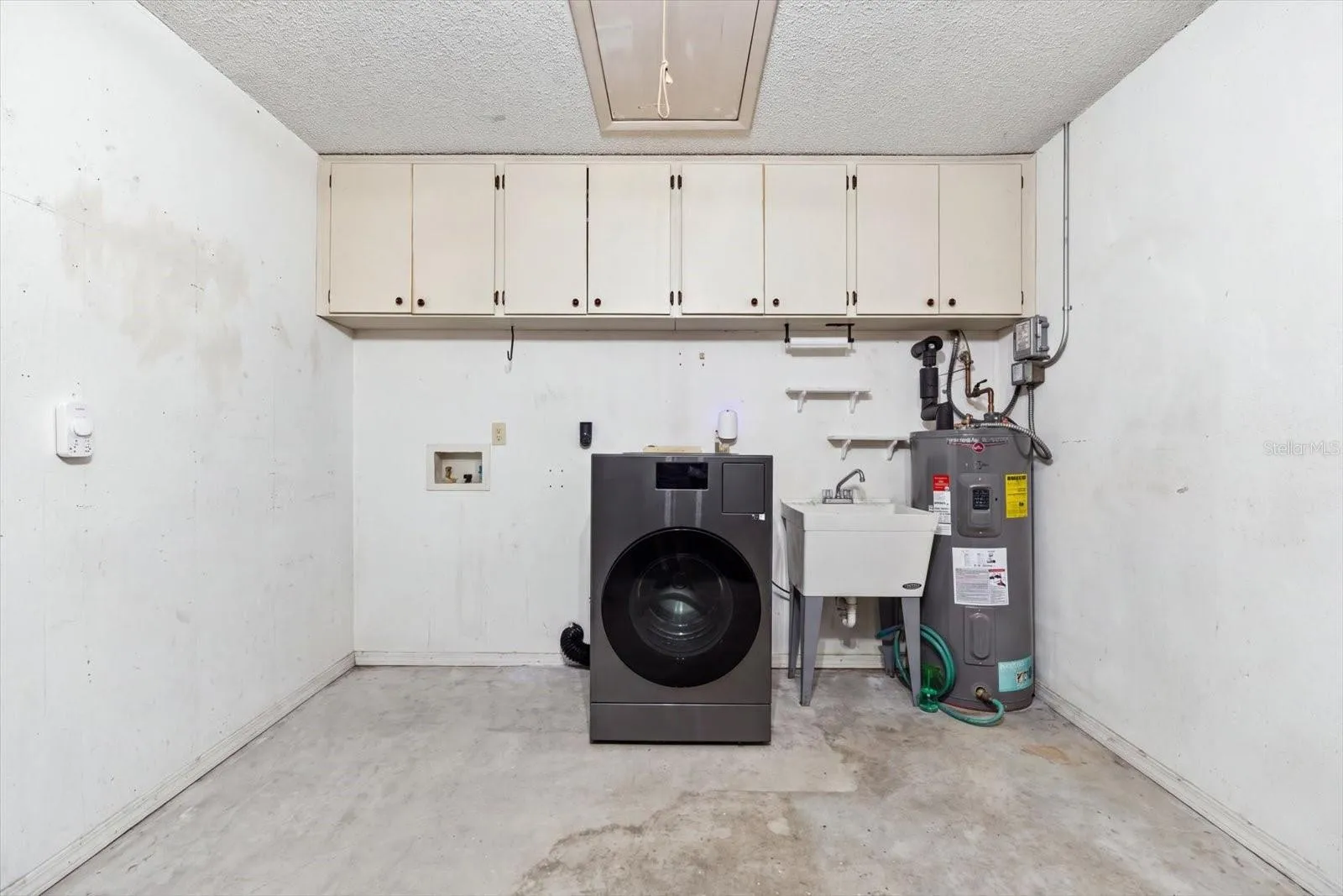 Garage with storage cabinets, washer/dryer combo, utility sink and water heater (2022). Newer Hurricane rated garage door 2023