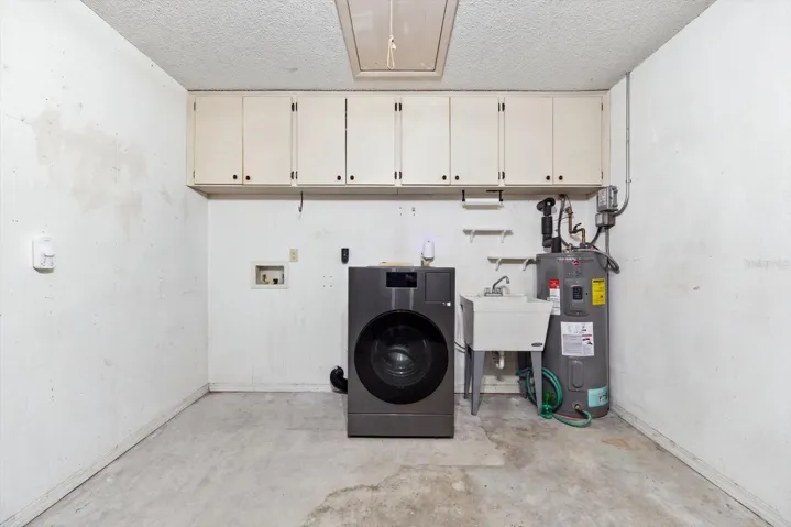 Garage with storage cabinets, washer/dryer combo, utility sink and water heater (2022). Newer Hurricane rated garage door 2023