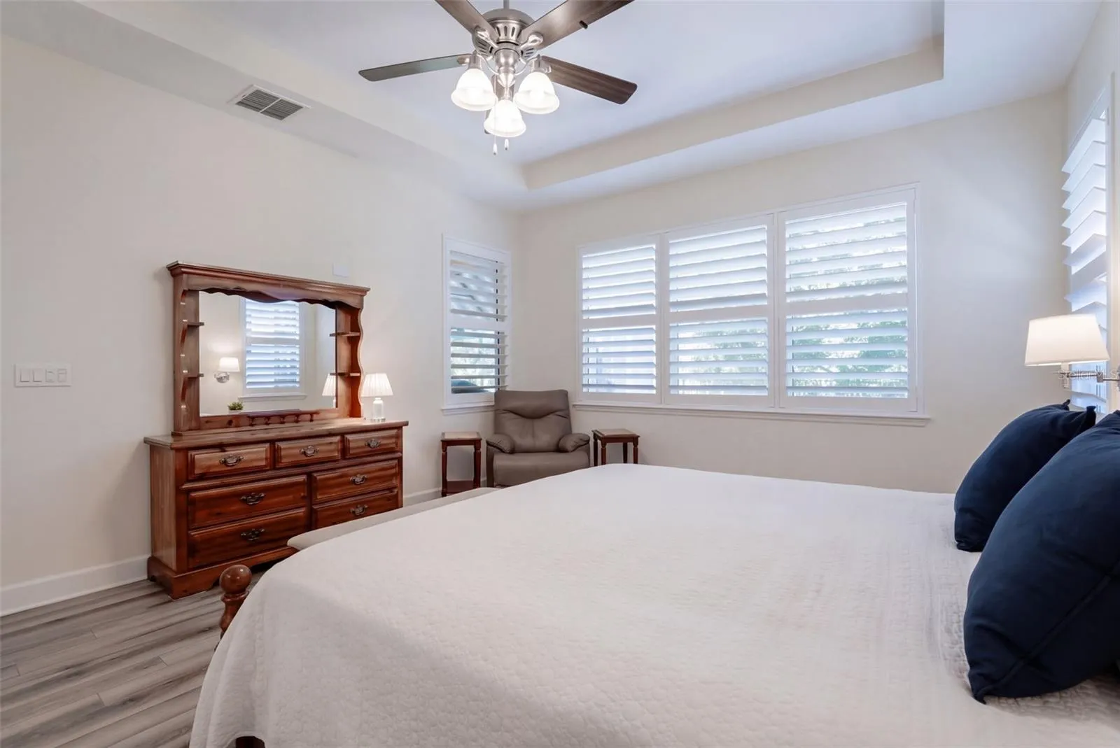 Primary Bedroom w/ Plantation style shutters, luxury vinyl floor, ceiling fan &amp; a wooded view