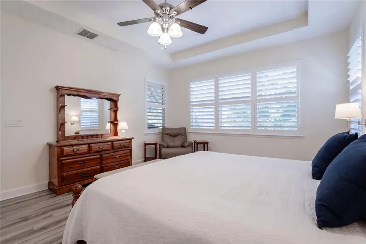 Primary Bedroom w/ Plantation style shutters, luxury vinyl floor, ceiling fan &amp; a wooded view