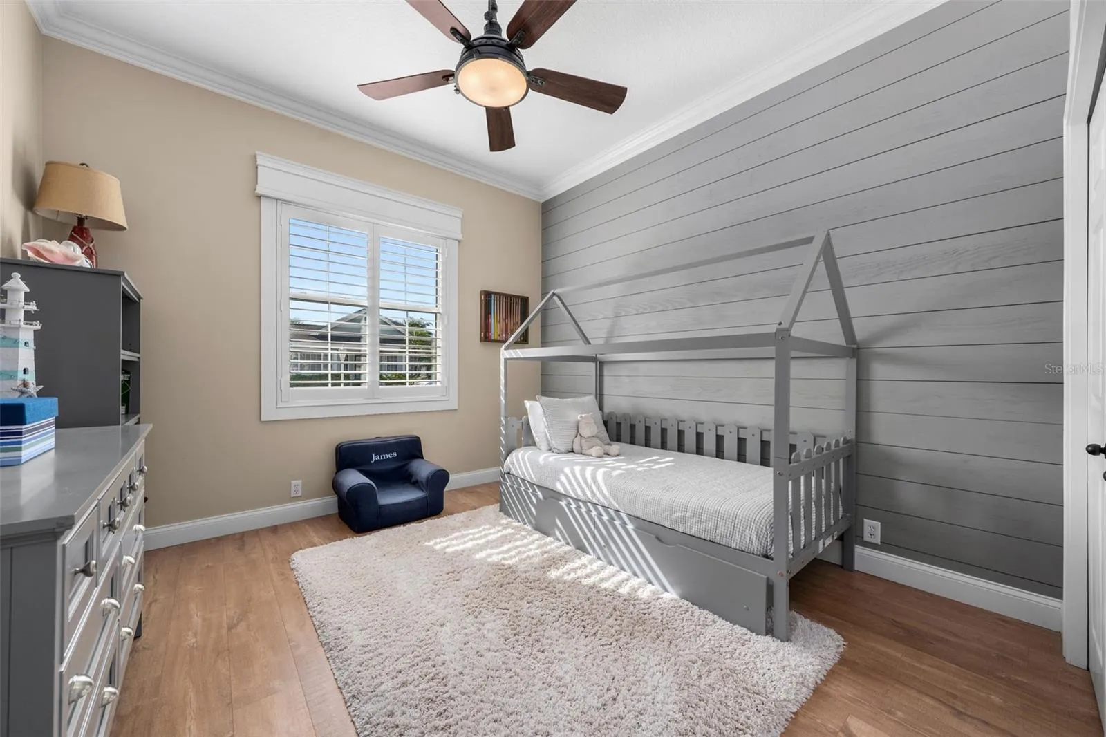 A shiplap feature wall adds character to this bright bedroom, complete with plantation shutters and crown molding.