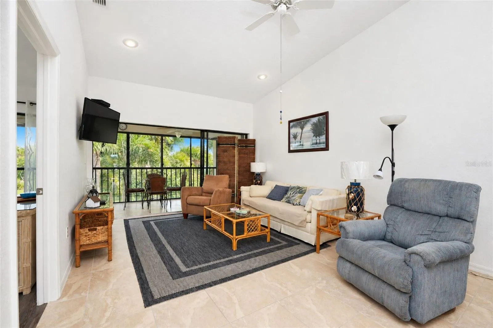 The living room has a cathedral ceiling, ceiling fan, tiled flooring and sliding glass doors to the lanai.