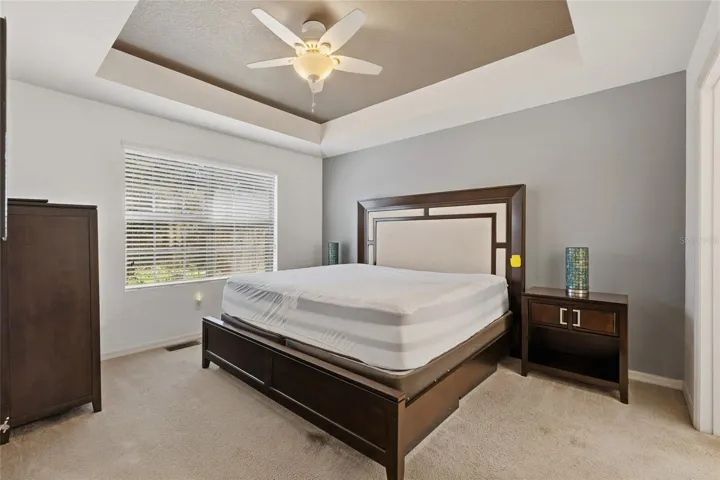 Primary bedroom featuring ceiling fan, accent ceiling with an ensuite bathroom