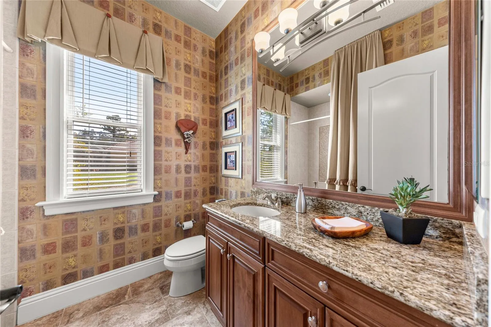Attractive bathroom featuring granite countertops, wood cabinetry, decorative wall finishes, and natural light.