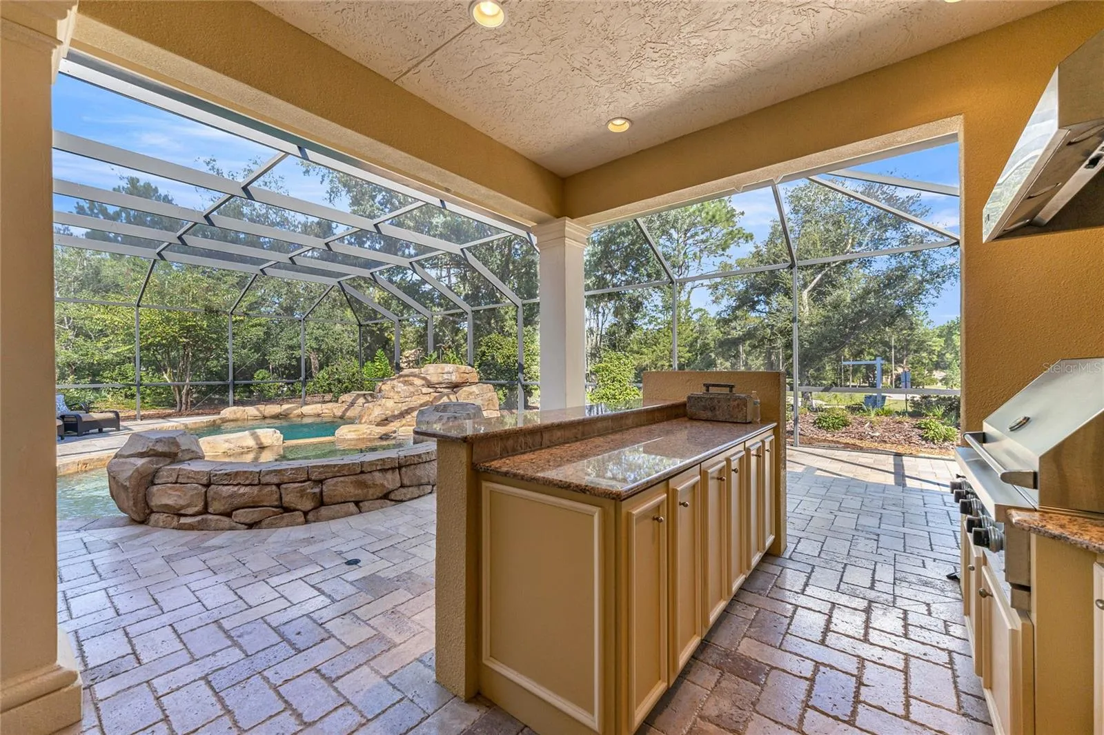 Impressive summer kitchen with built-in grill, granite countertops, sink, cabinetry, and poolside entertaining space.