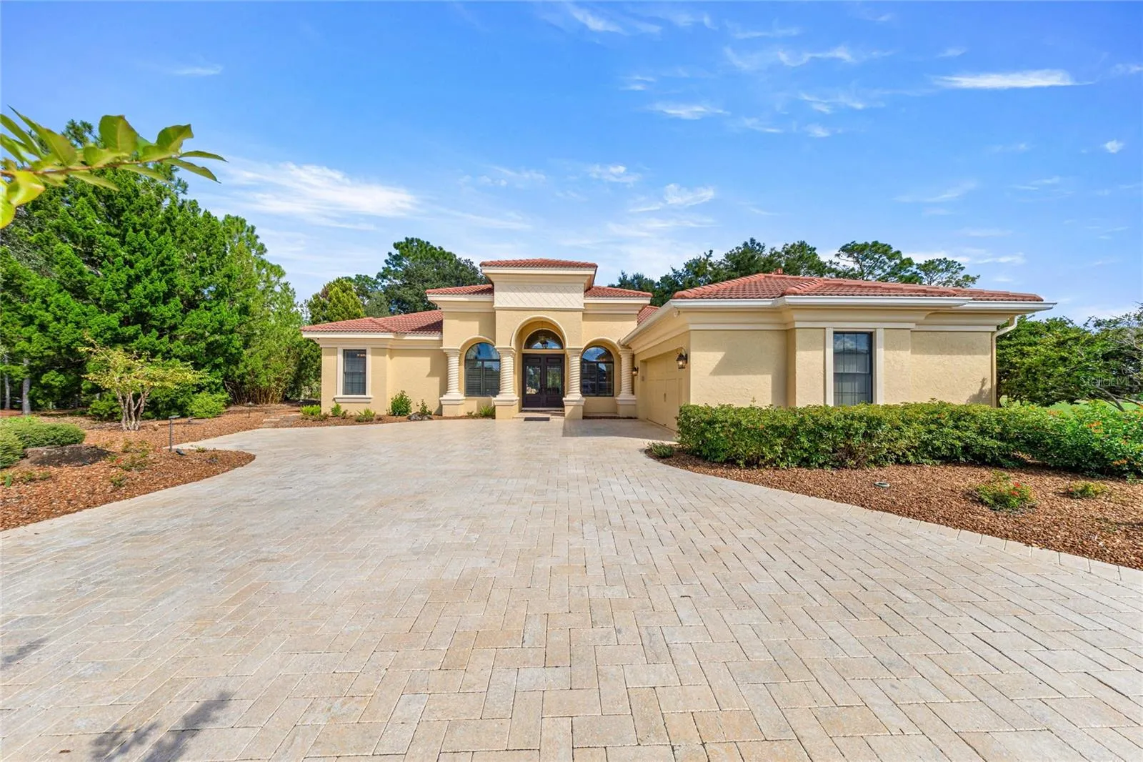 Beautiful Mediterranean-inspired home featuring a tile roof, elegant architectural detailing, grand covered entrance, and expansive paver driveway.