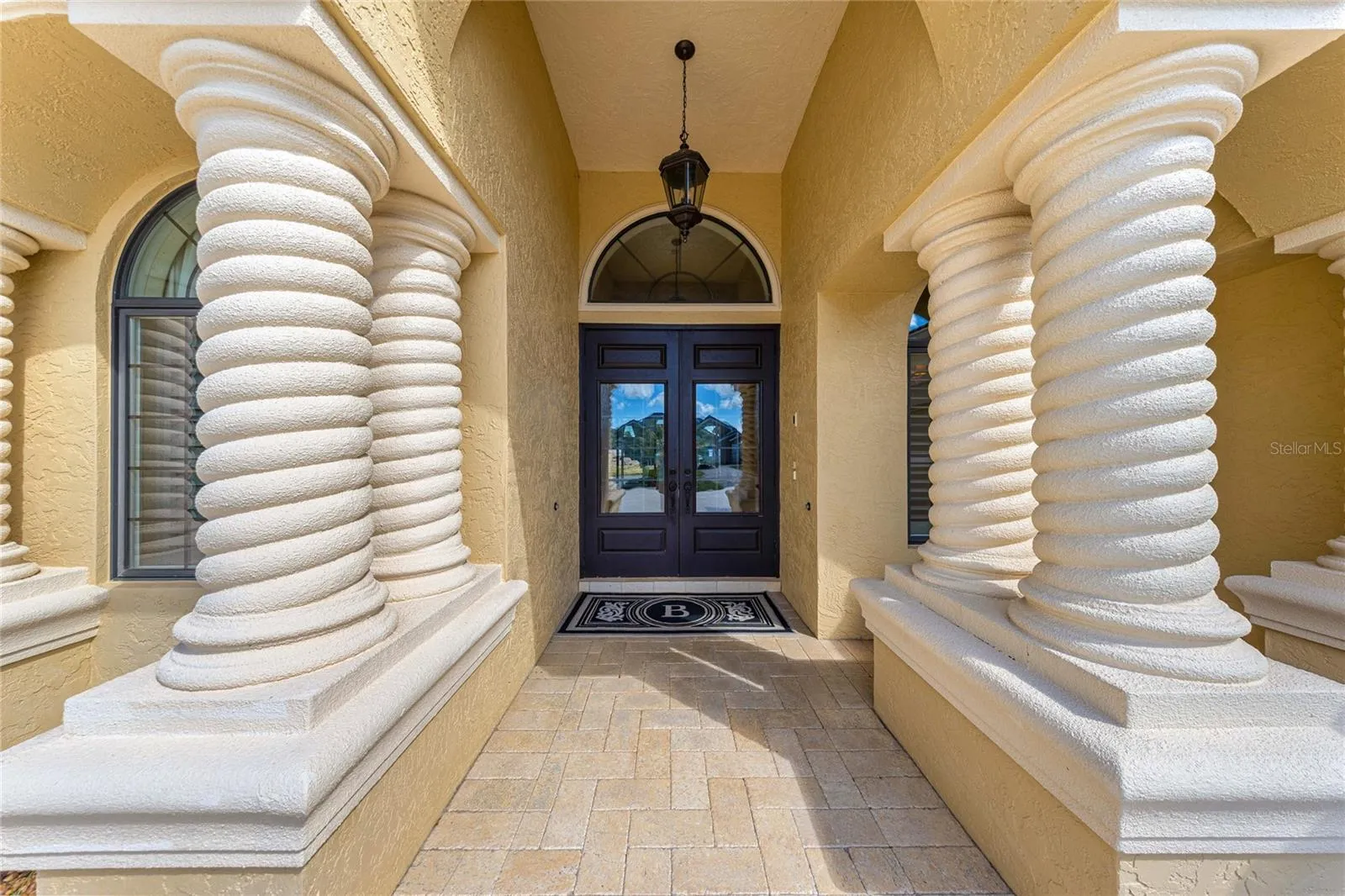 Impressive covered entryway featuring distinctive spiral columns, decorative arches, elegant double doors, and beautiful paver flooring.