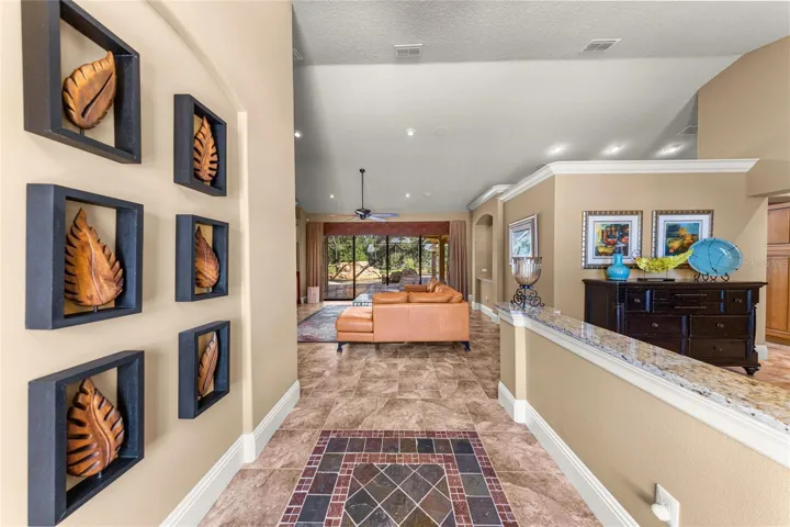 Welcoming foyer featuring decorative tile flooring, high ceilings, elegant crown molding, and an open view into the spacious living area with sliding glass doors overlooking the screened outdoor retreat.
