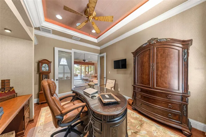 Private office or media room featuring a stunning illuminated tray ceiling, custom built-ins, and rich wood flooring.
