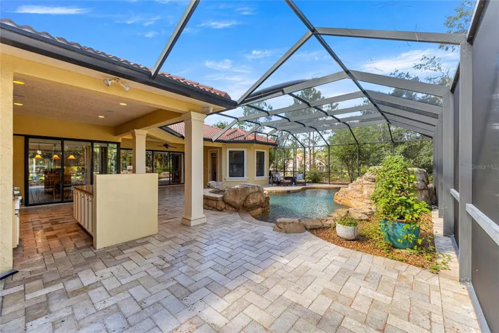 Expansive covered lanai with brick pavers, ceiling fan, and views of the custom pool and spa.