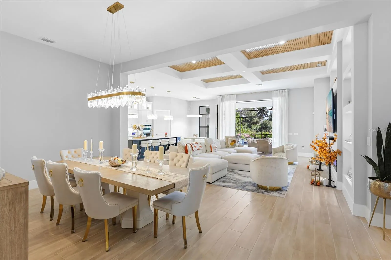 Bright, expansive open-concept living and dining areas featuring soaring ceilings, a coffered ceiling with inset wood trim, elegant architectural details, and expansive windows that fill the home with natural light.