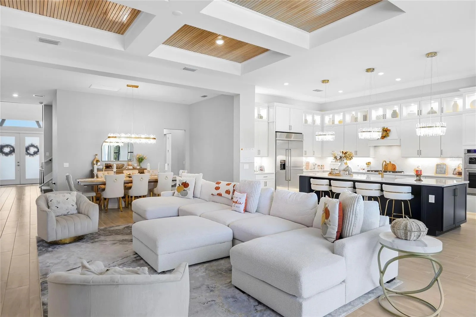 Bright, expansive open-concept living and dining areas featuring soaring ceilings, a coffered ceiling with inset wood trim, elegant architectural details, and expansive windows that fill the home with natural light.