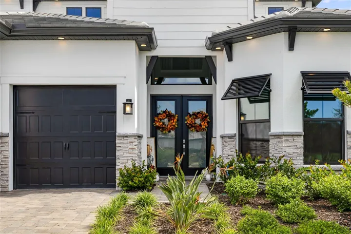 Elegant two-story residence featuring a striking modern coastal exterior, lush tropical landscaping, and an inviting paver driveway leading to a spacious three-car garage.