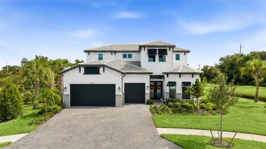 Elegant two-story residence featuring a striking modern coastal exterior, lush tropical landscaping, and an inviting paver driveway leading to a spacious three-car garage.